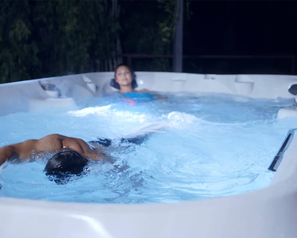 woman sitting in a corner and man swimming in jacuzzi swim spa