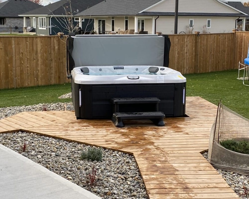 hot tub with a cover, placed on a wooden deck surrounded by a landscaped garden and wooden fence in a suburban backyard